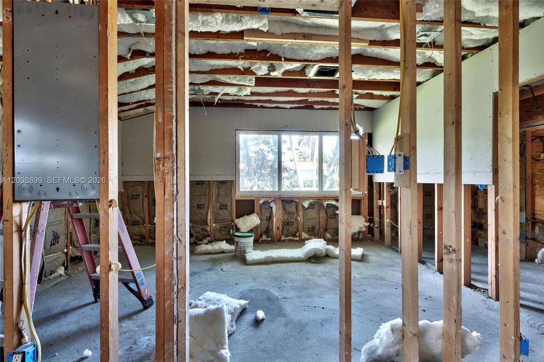 Interior space featuring exposed wood framing, batt insulation, concrete flooring, a multi-pane window, and an installed electrical panel