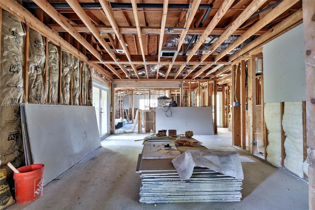 Open-concept interior featuring exposed wood ceiling joists, insulated timber stud walls, and glass panel doors