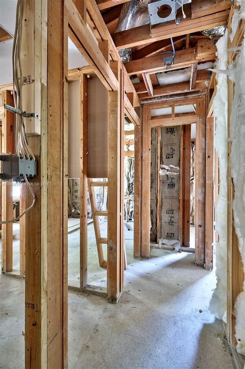 Interior structure featuring exposed wooden wall studs, concrete flooring, exposed ceiling rafters, and installed fiberglass insulation