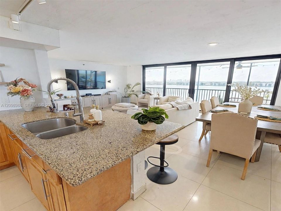 Kitchen featuring a stone countertop, dual-basin stainless steel sink, and high-arch faucet, complemented by large-format tile flooring and extensive floor-to-ceiling windows
