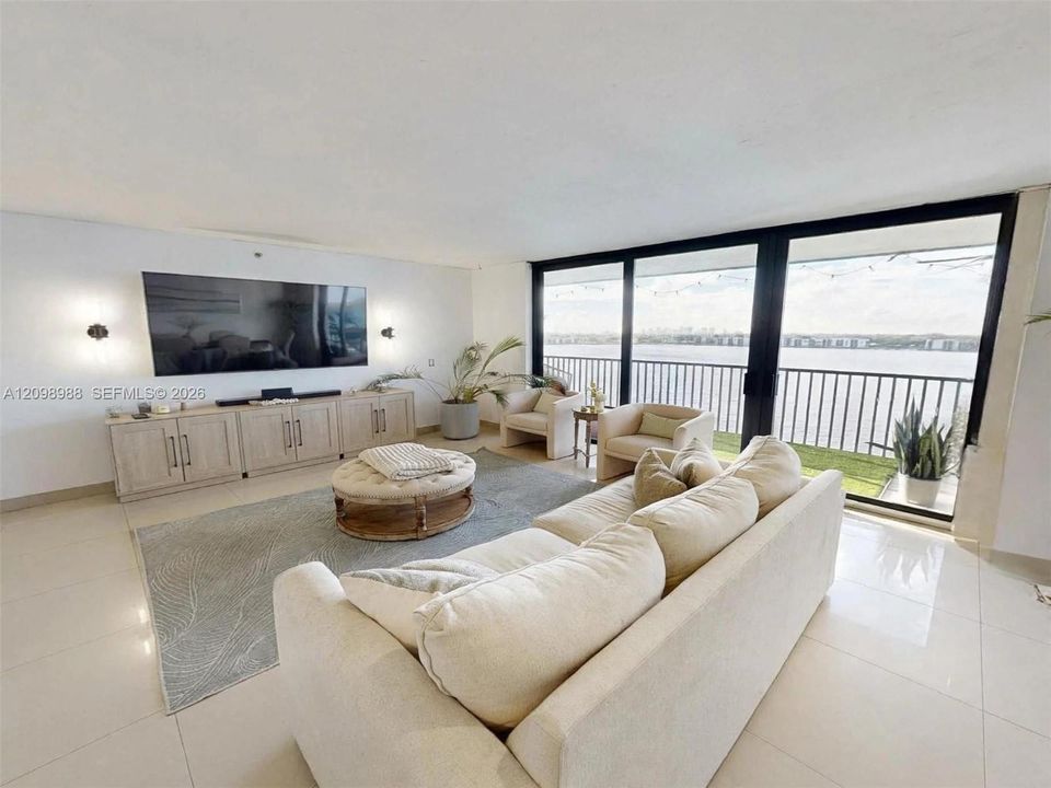 Living area featuring floor-to-ceiling glass sliding doors, integrated cabinetry, polished tile flooring, and a metal-railed balcony with waterfront exposure