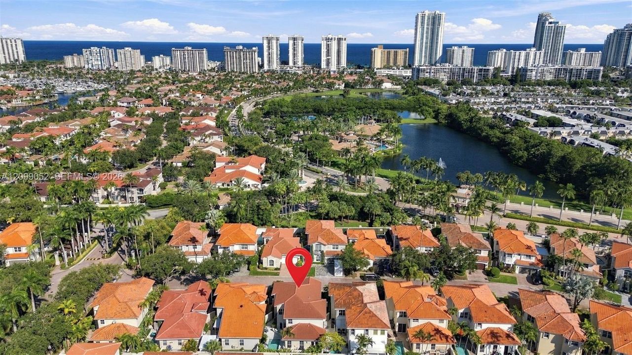 Aerial perspective of residential community featuring tiled roofs, manicured landscaping, integrated water features, and proximity to the coastline