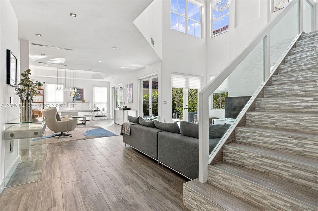Double-height ceiling, glass-paneled staircase railing, stacked stone-texture stair risers, wood-finish flooring, and multiple sets of French doors