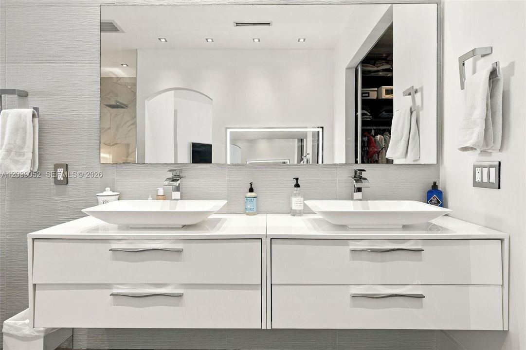 Floating dual vanity featuring white cabinetry, rectangular vessel sinks, chrome faucets, and large wall-mounted mirror with recessed lighting