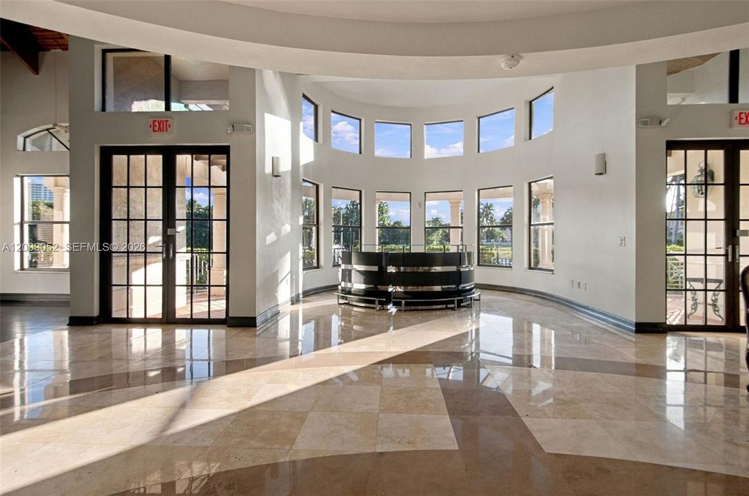 Rotunda interior featuring polished stone flooring, a multi-paneled curved window wall, and dual glass-paned double doors