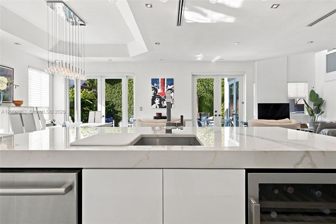 Kitchen island featuring a stone-look countertop, undermount sink with a high-arch faucet, built-in stainless steel dishwasher, integrated wine refrigerator, and minimalist flat-panel cabinetry