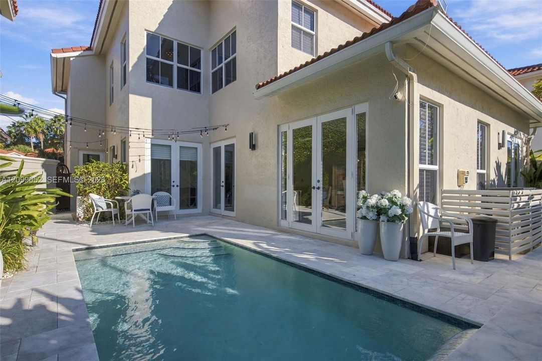 Stucco exterior featuring a rectangular inground pool, stone-paver decking, multiple sets of glass double doors, and a tile roof