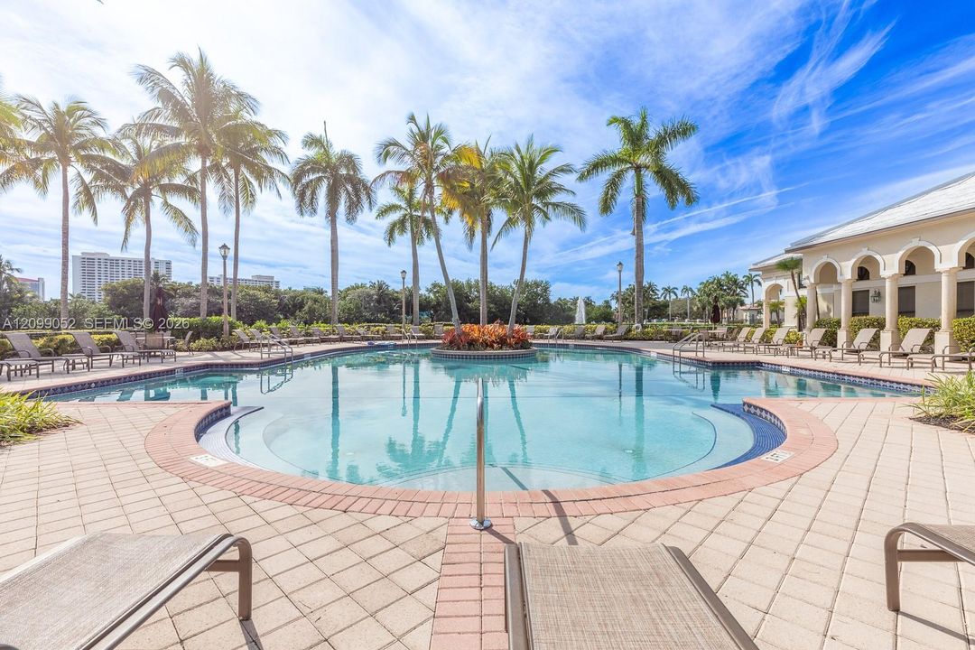 In-ground swimming pool featuring a curved perimeter, stepped entry, central garden island, and surrounding paver patio with a colonnade structure