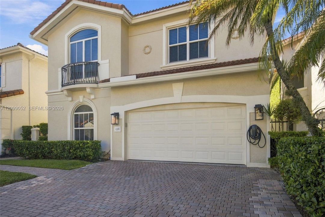 Stucco exterior featuring a paver driveway, arched windows, decorative metal balcony, and tile roofing