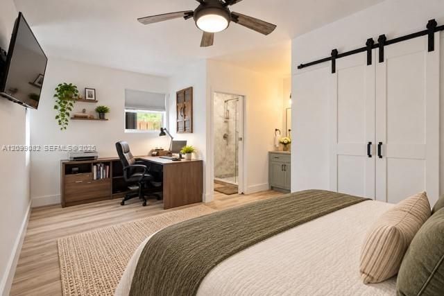 Interior space featuring wood-finish flooring, a ceiling fan, white sliding barn doors with matte black hardware, and an en-suite bathroom with a glass-enclosed shower