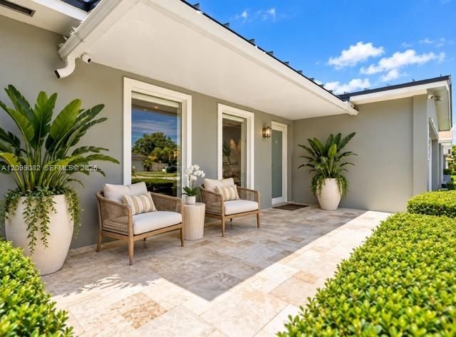Covered entryway featuring natural stone patio flooring, neutral-toned exterior siding, tall windows, and exterior wall-mounted lighting