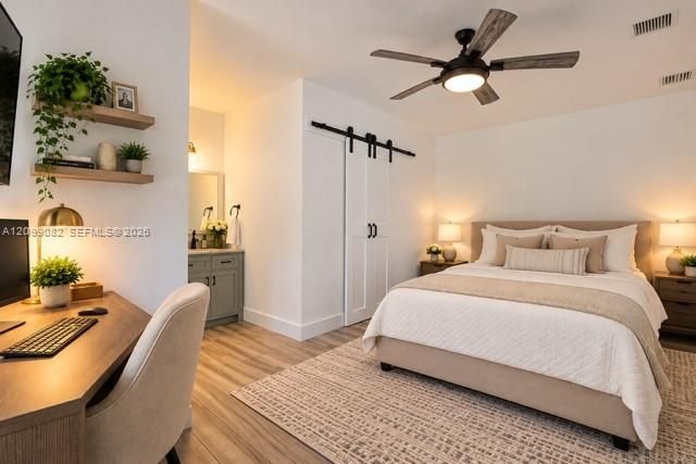 Wood-finish flooring, white sliding barn door with black hardware, ceiling fan with integrated lighting, and built-in wall shelving