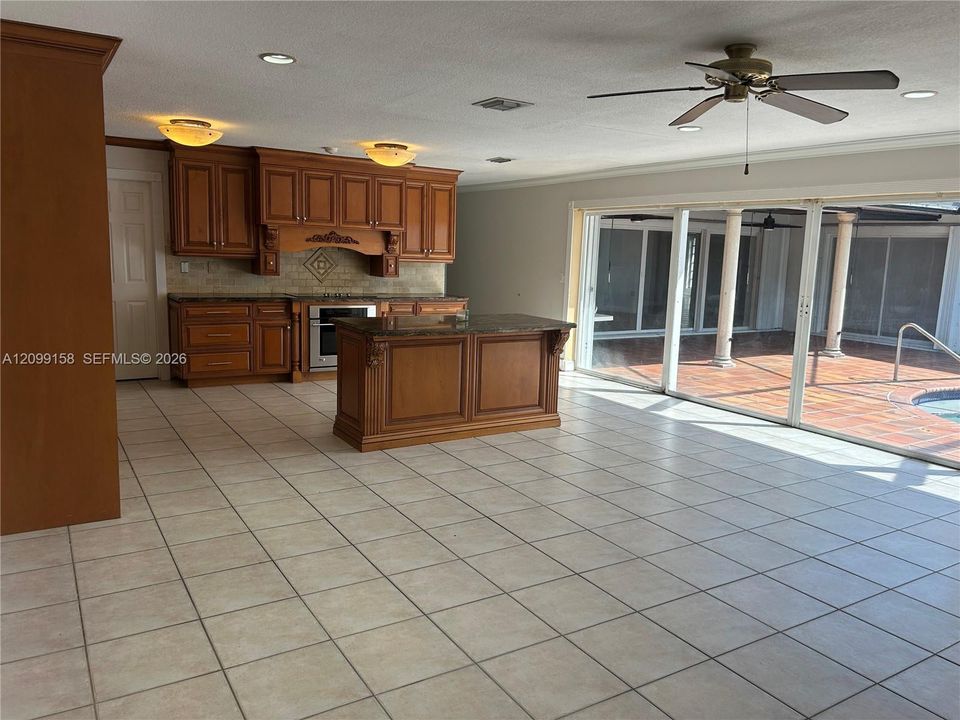 Kitchen featuring custom wood cabinetry, central island, stone-surface countertops, tile flooring, and multi-panel sliding glass doors