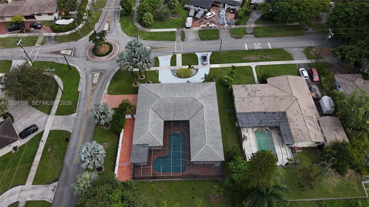 Aerial perspective of a residence featuring a concrete tile roof, a screened-in swimming pool enclosure, and a paved walkway