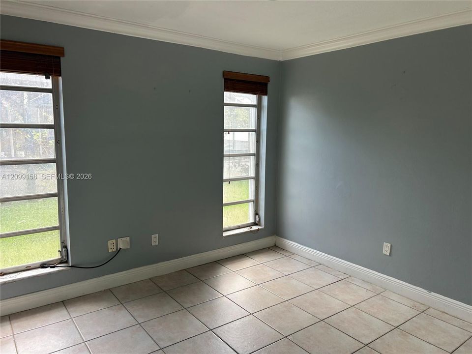 Room featuring neutral-toned ceramic tile flooring, crown molding, and two multi-pane windows with horizontal wood-finish blinds
