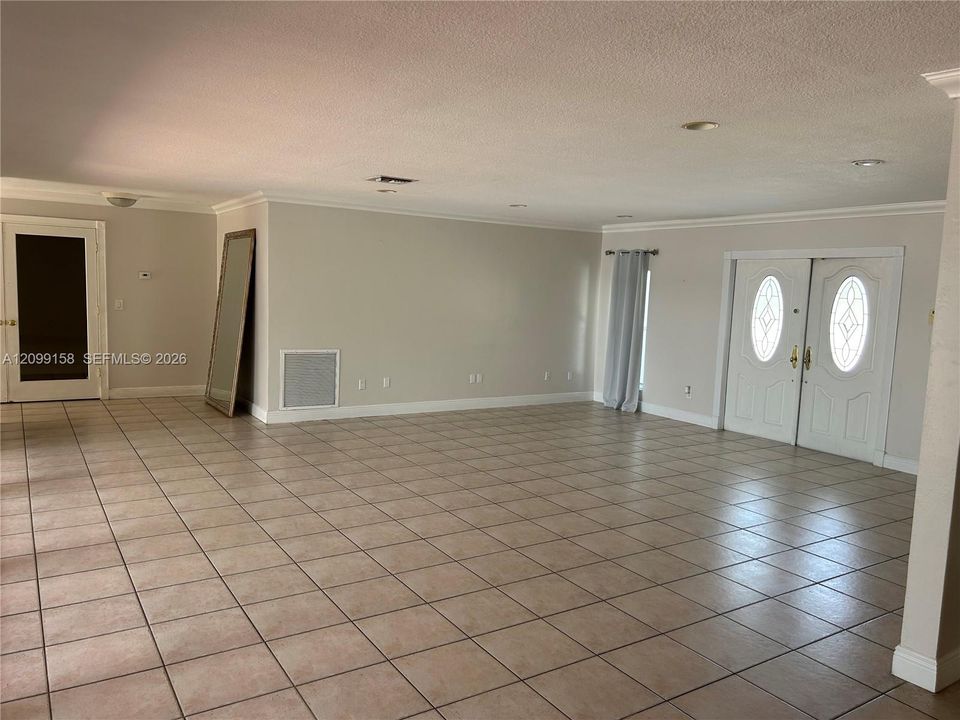 Spacious open-concept living area with tile flooring throughout, recessed ceiling lighting, and multiple glass doors with sidelights providing natural illumination