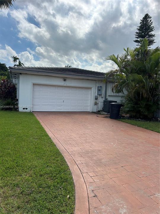 Attached two-car garage with a white roll-up door, complemented by a textured paved driveway and manicured lawn
