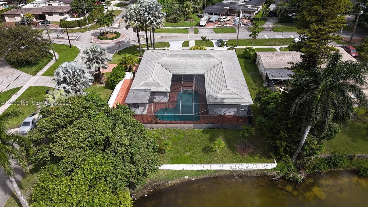 Aerial perspective of a single-story residence featuring a screened-in pool enclosure, tiled patio, concrete tile roof, and waterfront location with mature landscaping
