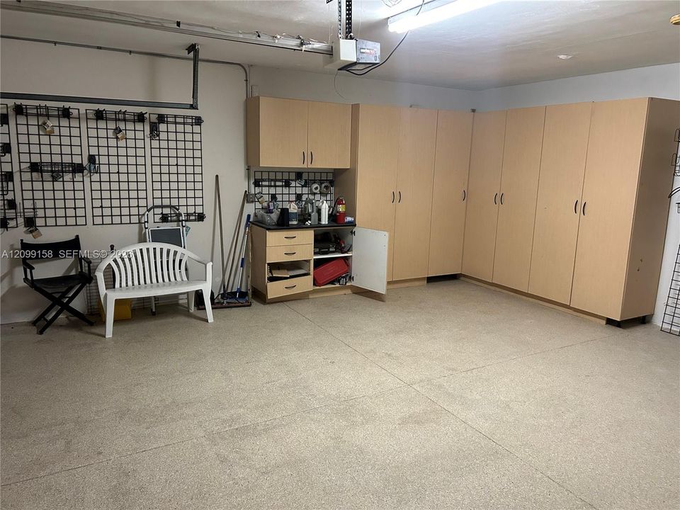 Garage featuring an epoxy floor coating, expansive wall-to-wall light wood-finish cabinetry, built-in storage drawers, and integrated wall-mounted wire grid organization panels
