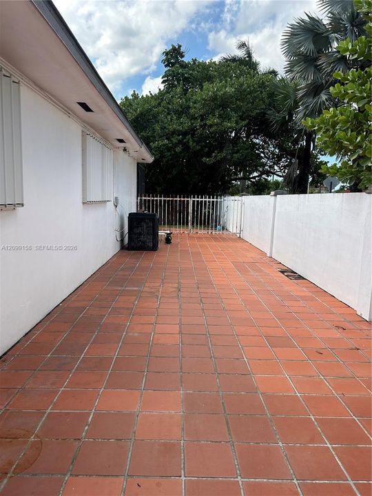 Exterior side patio featuring terracotta tile flooring, enclosed by a white masonry privacy wall and gated metal fencing