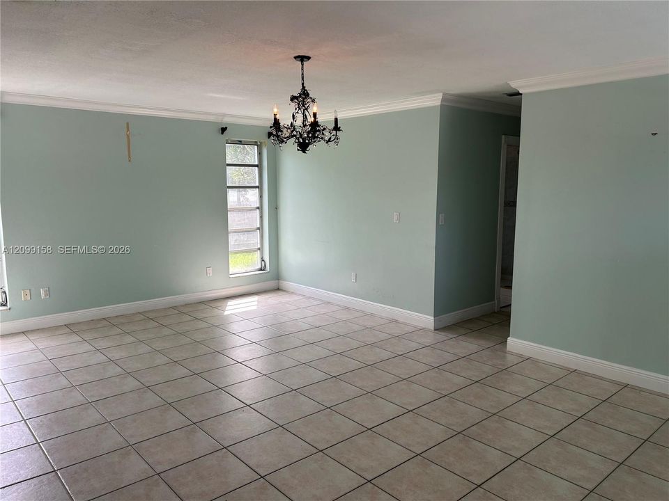 Spacious interior featuring large-format tile flooring, crown molding, multi-pane windows, and a decorative wrought iron chandelier