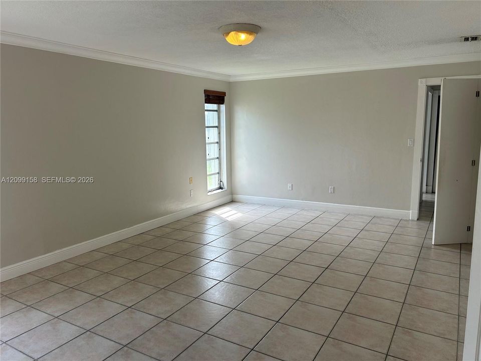 Interior space featuring neutral wall paint, tile flooring, crown molding, and a flush-mount ceiling light fixture