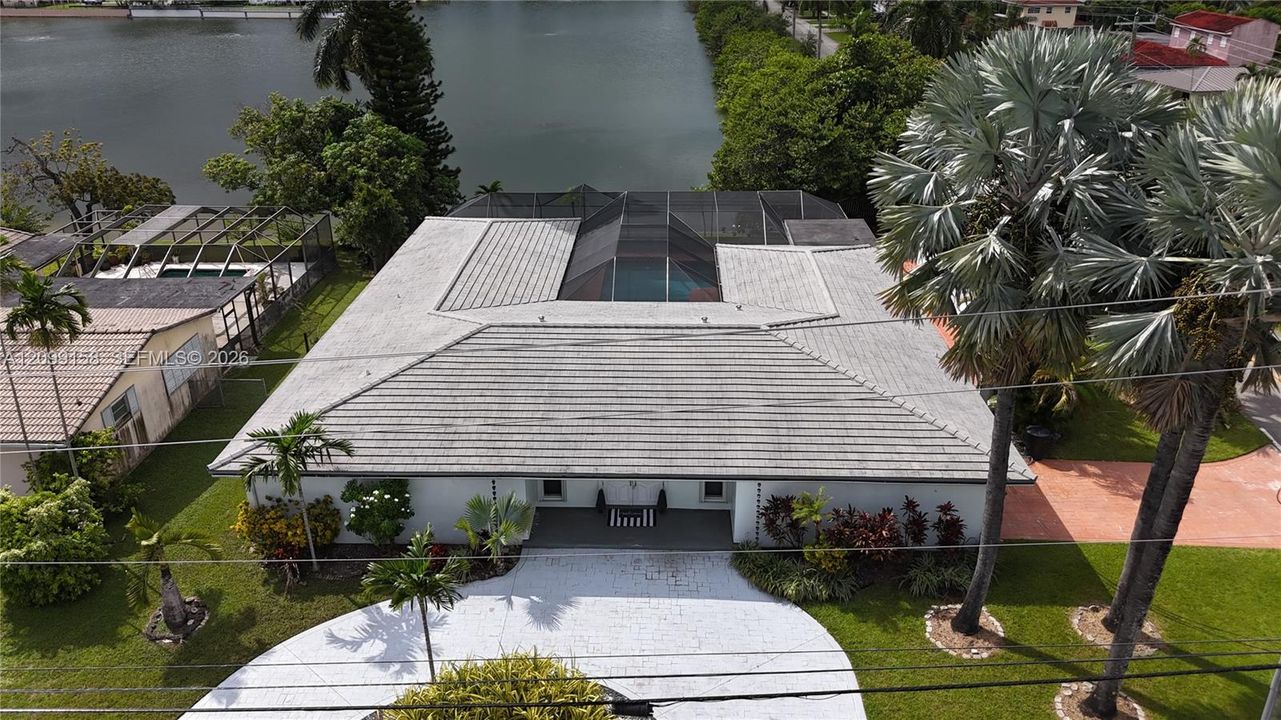 Waterfront property featuring a tiled roof, screened pool enclosure, paved circular driveway, and mature palm landscaping