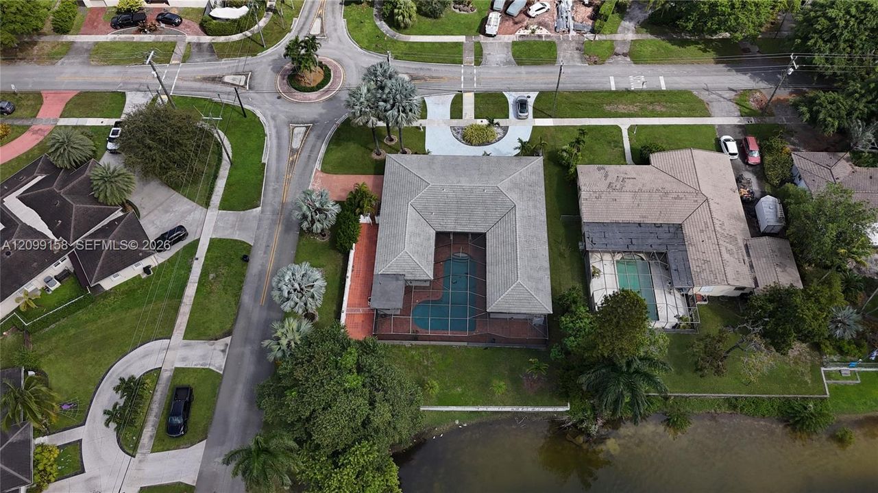 Aerial perspective featuring a U-shaped residence, screened-in swimming pool, paved entryway, and direct waterfront access