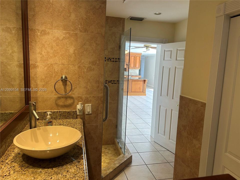 Stone-topped vanity featuring a vessel sink and single-handle faucet, tiled shower with glass enclosure, and large-format floor tiling