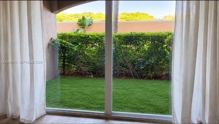 Floor-to-ceiling sliding glass door, private patio space, synthetic lawn, and mature privacy hedging
