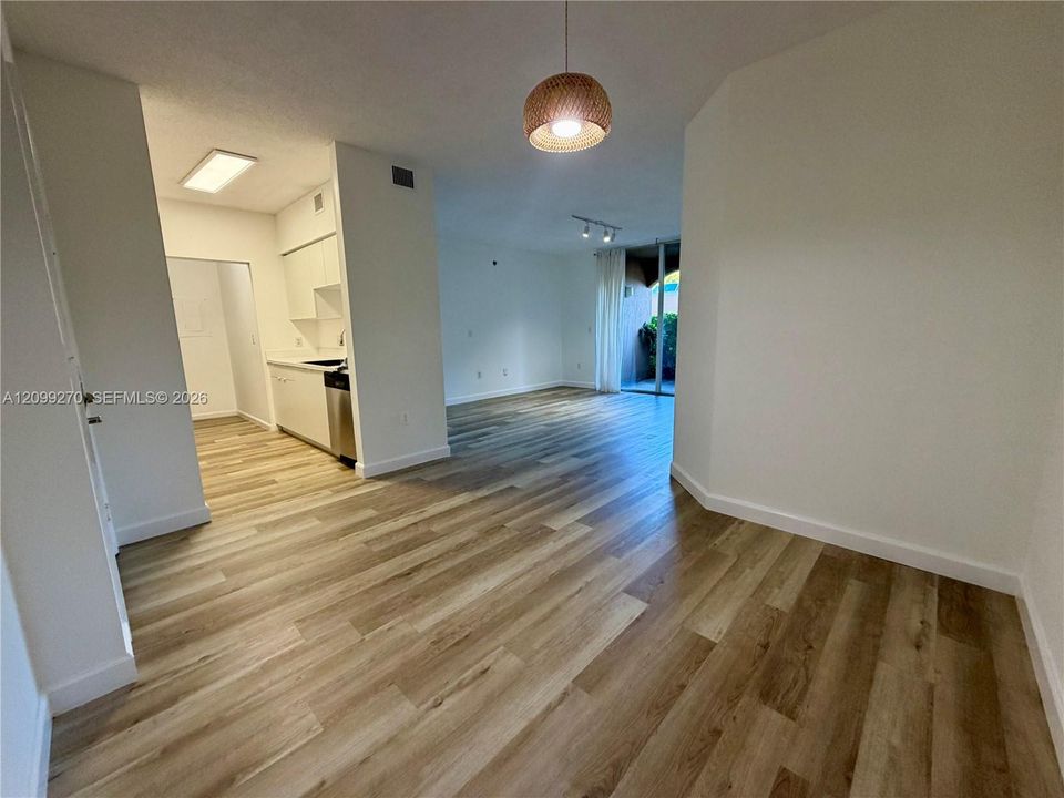 Open interior featuring wood-finish flooring, a kitchen with white cabinetry, a natural-textured dome pendant light, and a sliding glass door