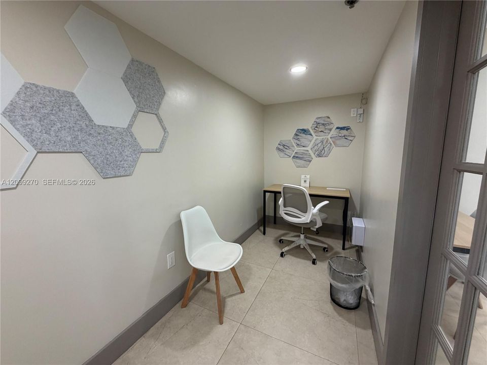Enclosed space featuring large-format tile flooring, recessed ceiling lighting, decorative wall-mounted acoustic hexagonal panels, and a glass-paned door