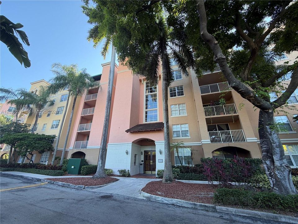 Multi-story stucco exterior featuring stacked balconies, multi-pane windows, and a covered building entrance with wood-frame doors