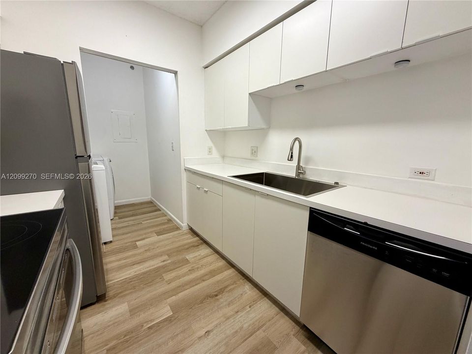 Kitchen featuring white flat-panel cabinetry, solid-surface countertops, a stainless steel undermount sink with a gooseneck faucet, stainless steel dishwasher, and wood-finish flooring