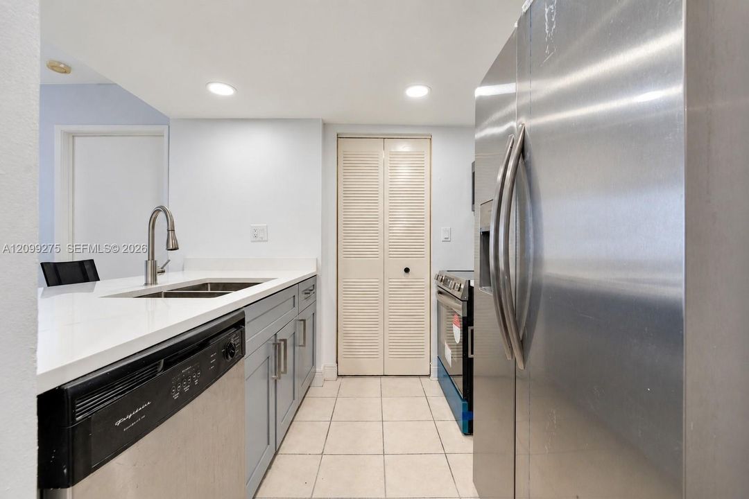 Bright kitchen and entryway featuring a breakfast bar with two stools, white countertops, stainless steel appliances, recessed lighting, and tiled flooring.