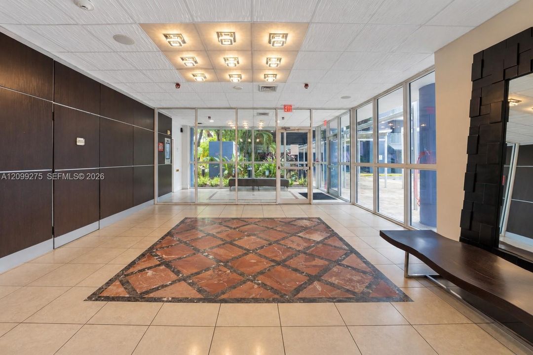 Elegant building lobby featuring decorative marble flooring, modern lighting, glass entry doors, and a welcoming reception-style seating area.