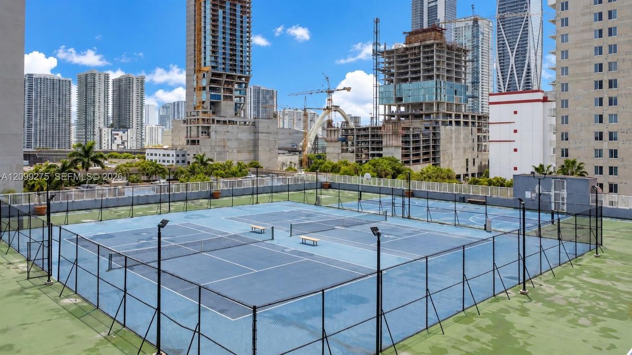 Recreational tennis courts with secure fencing, expansive city skyline views, and surrounding high-rise developments, offering residents an elevated outdoor sports and leisure experience.