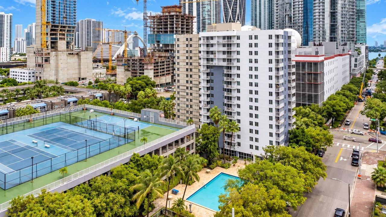 Enjoy resort-style amenities including a swimming pool and sports courts, surrounded by lush tropical landscaping and a vibrant urban skyline.