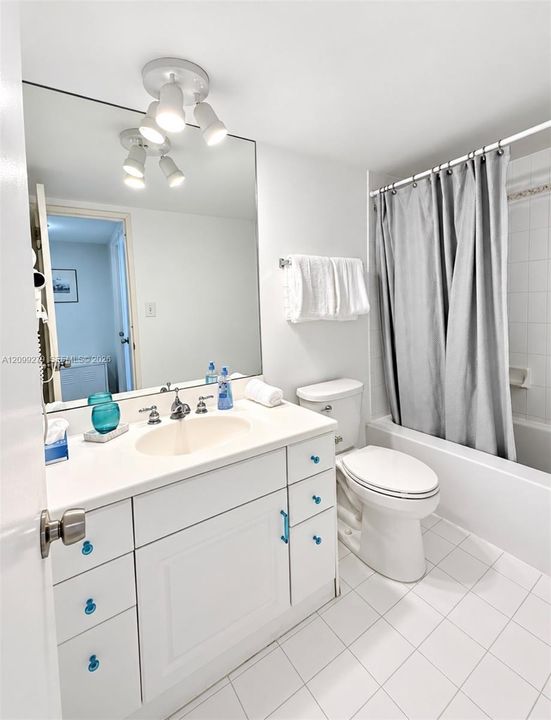 Bathroom featuring a white vanity with integrated sink, large wall-mounted mirror, multi-light ceiling fixture, and a tiled shower surround