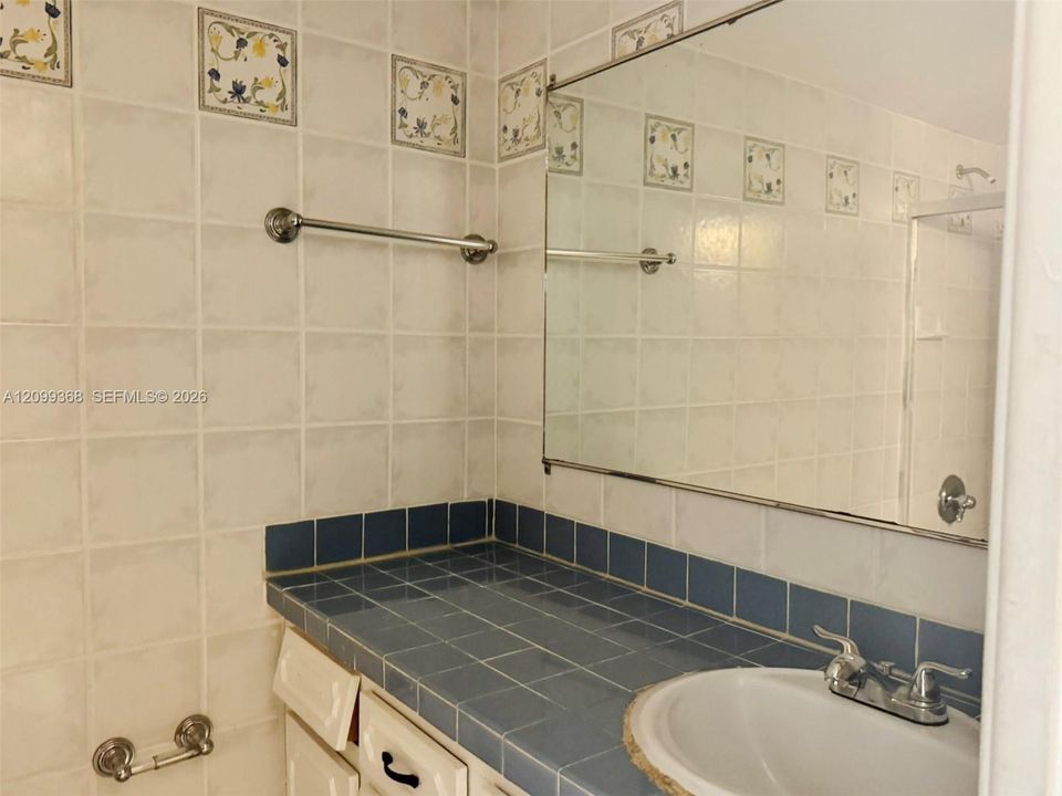 Bathroom featuring square tile backsplash in a blue finish, integrated vanity countertop with an inset basin, chrome fixtures, decorative patterned accent tiles, and a large wall-mounted mirror