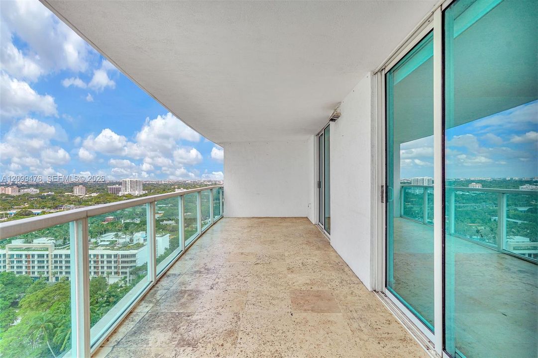 Covered balcony featuring stone tile flooring and glass panel railings