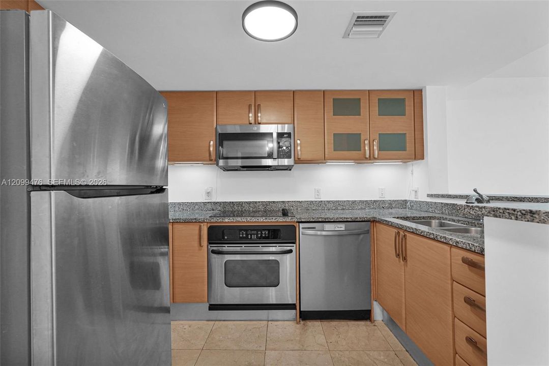 Kitchen featuring wood cabinetry, stone countertops, stainless steel appliances, under-cabinet lighting, and tile flooring