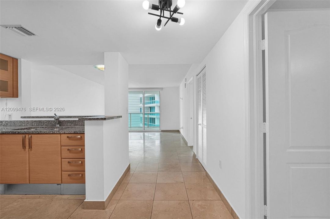 Kitchen featuring wood-finish cabinetry, stone-surfaced countertops, neutral tile flooring, louvered closet doors, and a multi-bulb geometric light fixture
