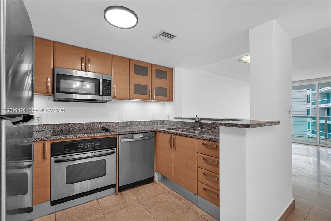 Kitchen featuring wood-finish cabinetry, stone-surface countertops, stainless steel appliances, and tiled flooring