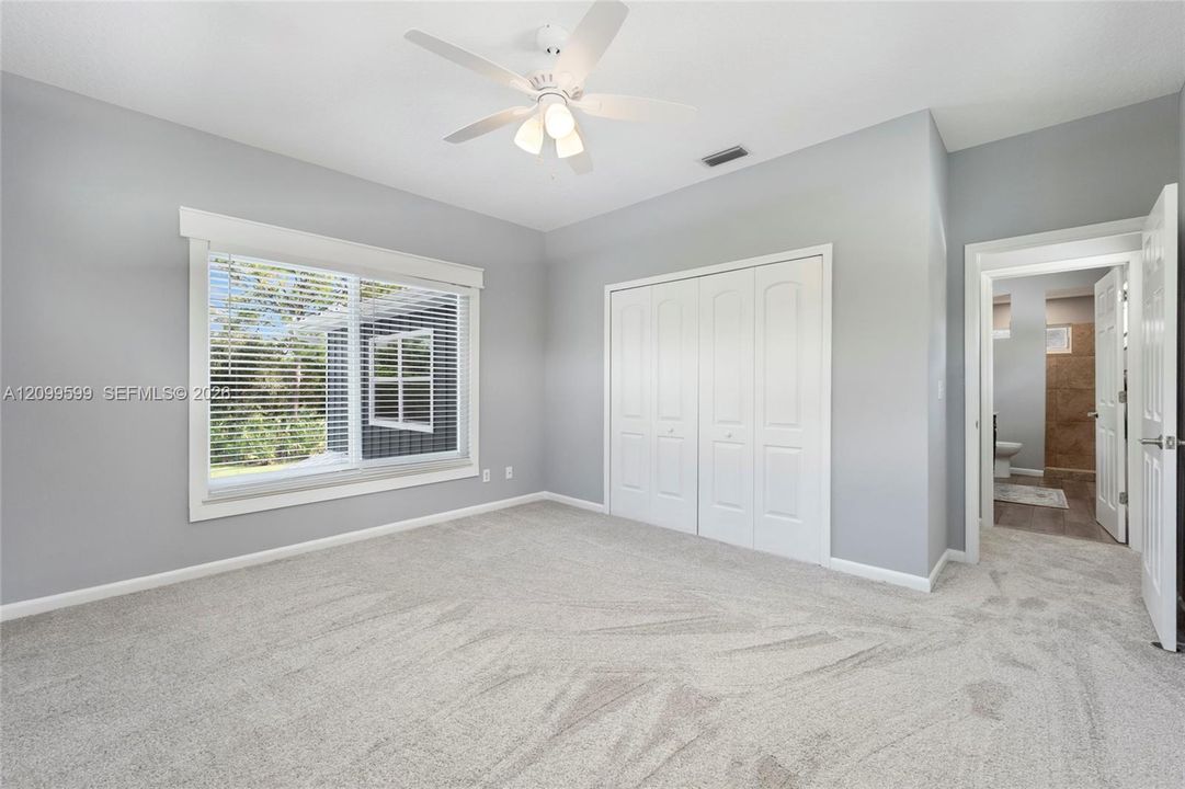 Neutral wall color, carpeted flooring, large window with blinds, bi-fold closet doors, and a ceiling fan with integrated lighting