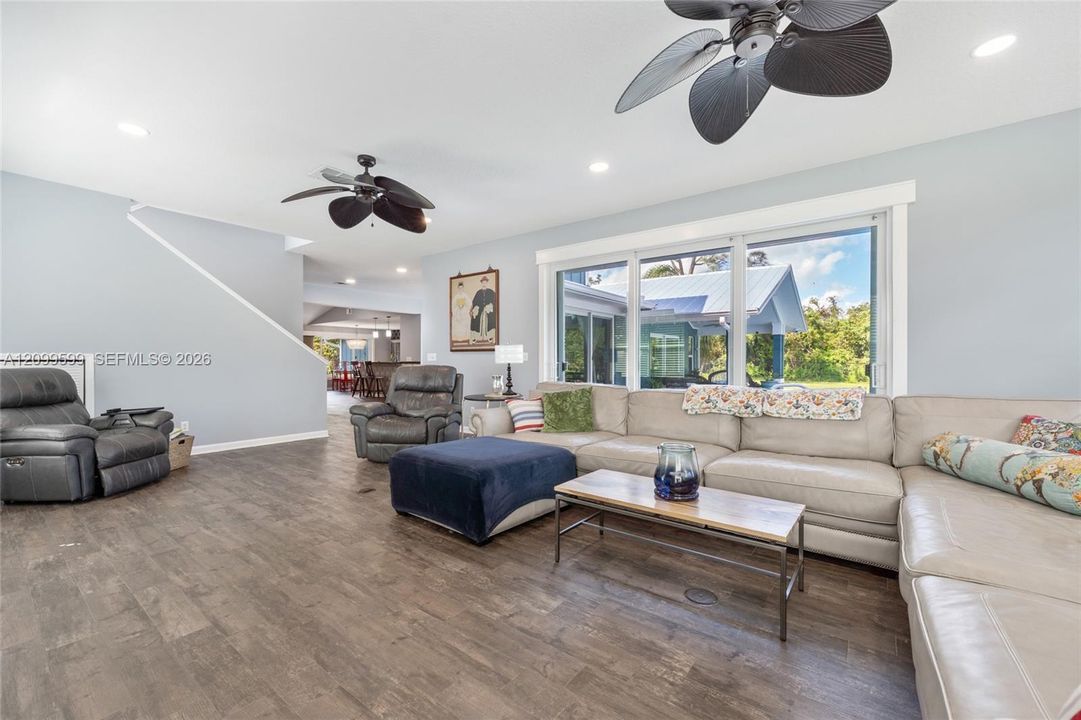 Living area featuring wood-finish flooring, recessed lighting, and dual ceiling fans with matte black finishes, complemented by a large multi-pane window