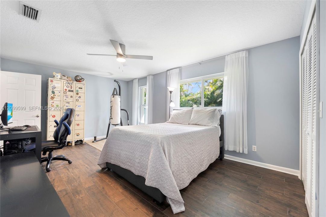 Bedroom featuring dark wood-finish flooring, a contemporary brushed-nickel ceiling fan, multi-pane windows, and white louvered closet doors