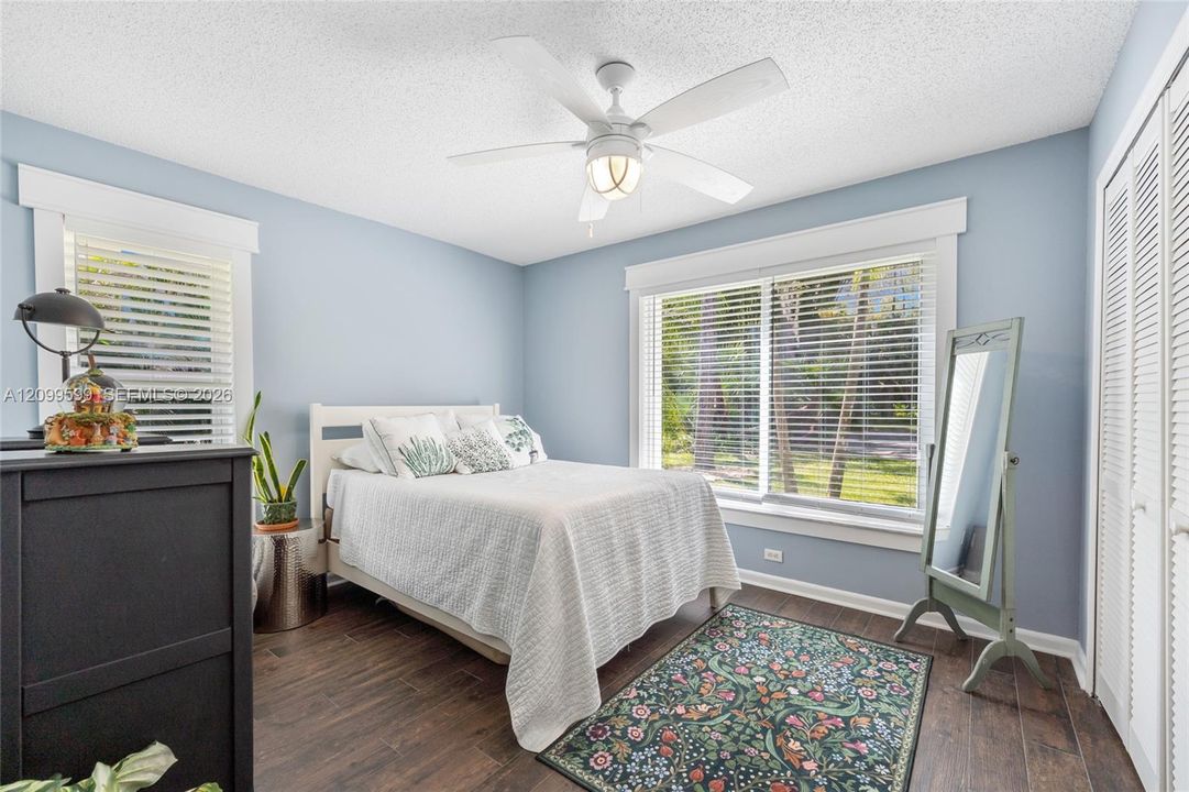 Room with wood-finish flooring, white ceiling fan with integrated light fixture, dual windows with blinds, and white louvered closet doors