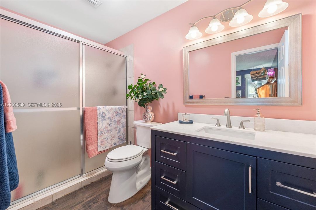 Dark navy shaker-style vanity with a light-toned countertop, undermount sink, brushed nickel hardware, and a glass-enclosed shower featuring a framed sliding door