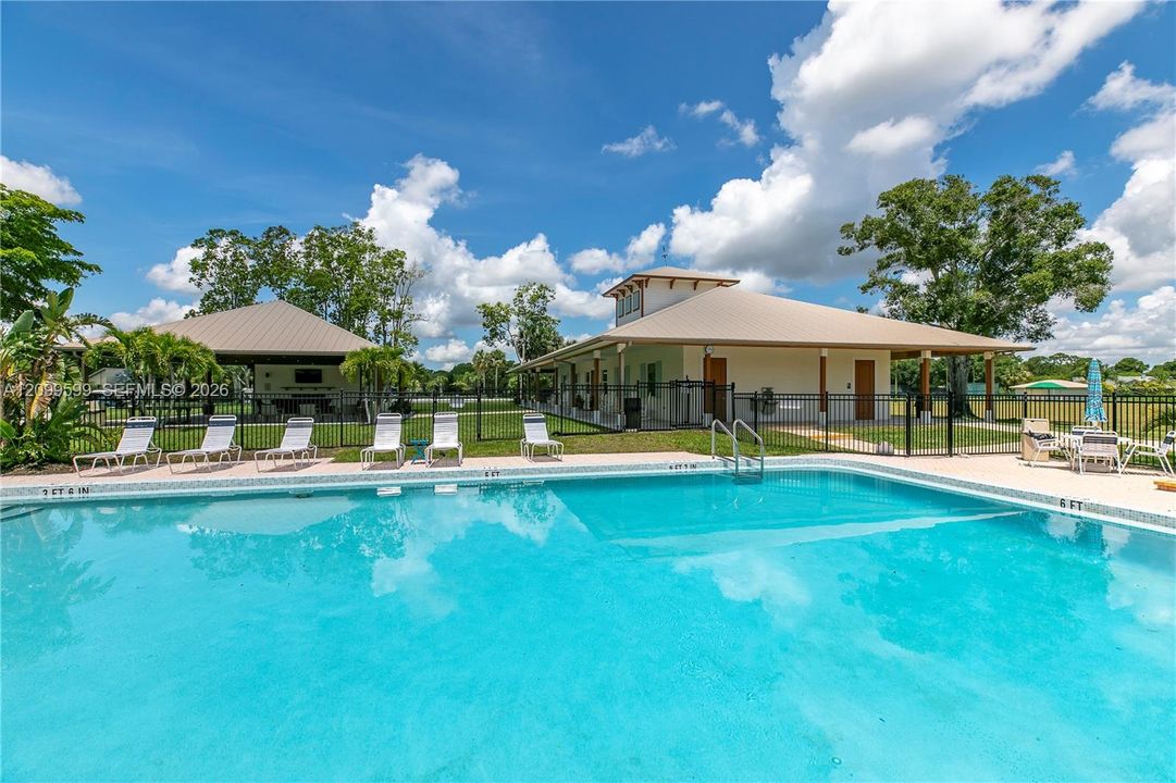 In-ground swimming pool featuring tile coping and metal safety fencing, accompanied by a covered pavilion, multi-structure exterior with metal roofing, and surrounding lawn